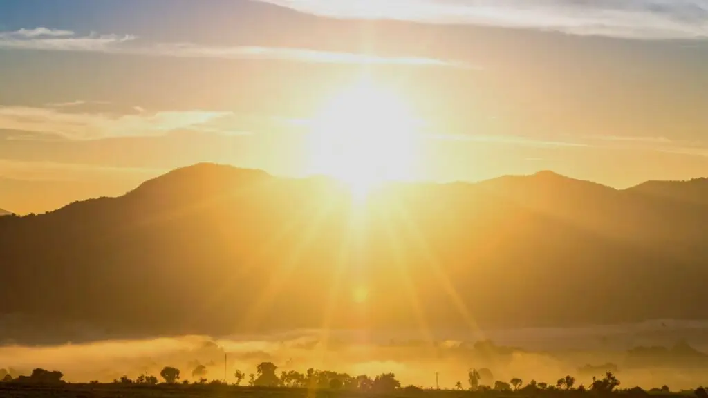 Golden sunrise breaking over distant mountains, casting warm light across a quiet landscape