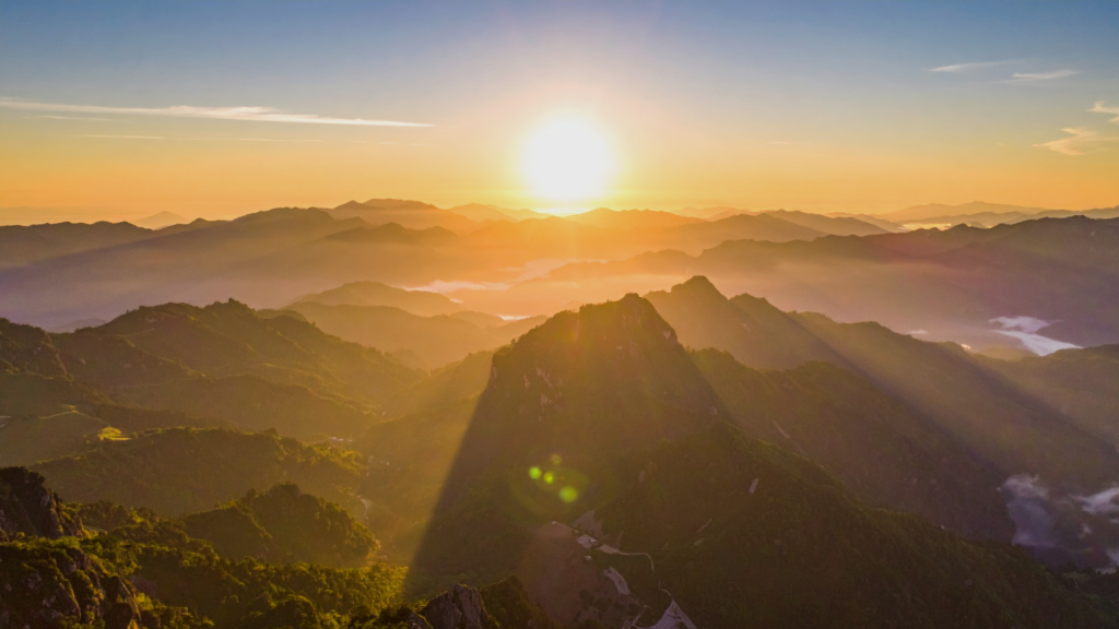 Sunrise-breaking-over-layered-mountain-ridges-casting-warm-light-across-a-quiet-landscape.